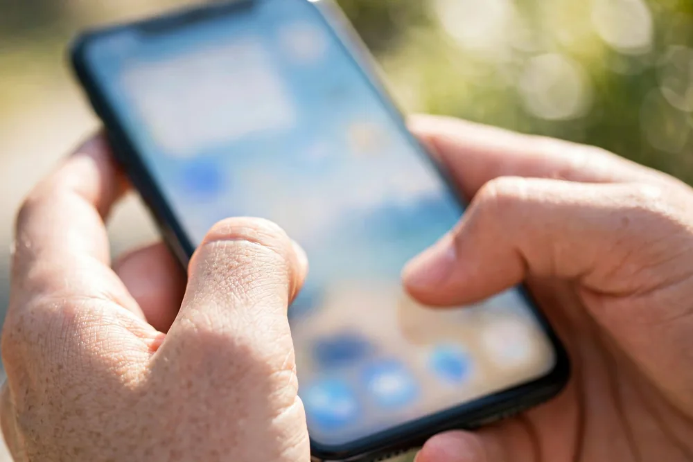 Close-up of hands typing a message on a smartphone keyboard in bright daylight